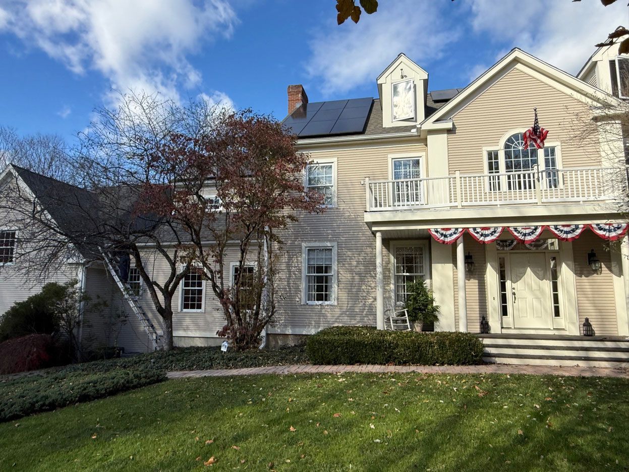 A two-story, cream-colored house with a front porch, red-white-and-blue bunting, and a lawn under a partly cloudy sky.
