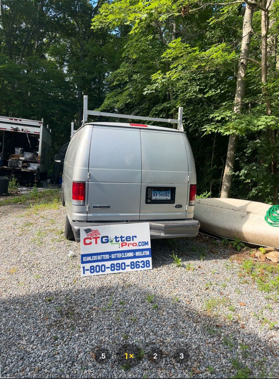 A silver work van parked on a gravel lot in front of trees, with a 