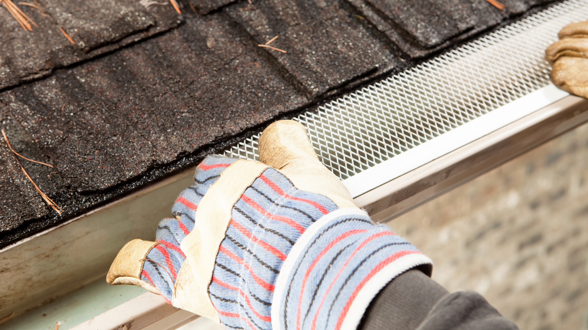 Person in a red jacket on a ladder cleaning a roof gutter against a blue sky