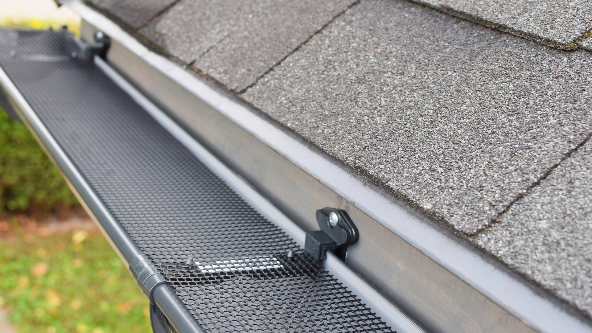 Person in a red jacket on a ladder cleaning a roof gutter against a blue sky