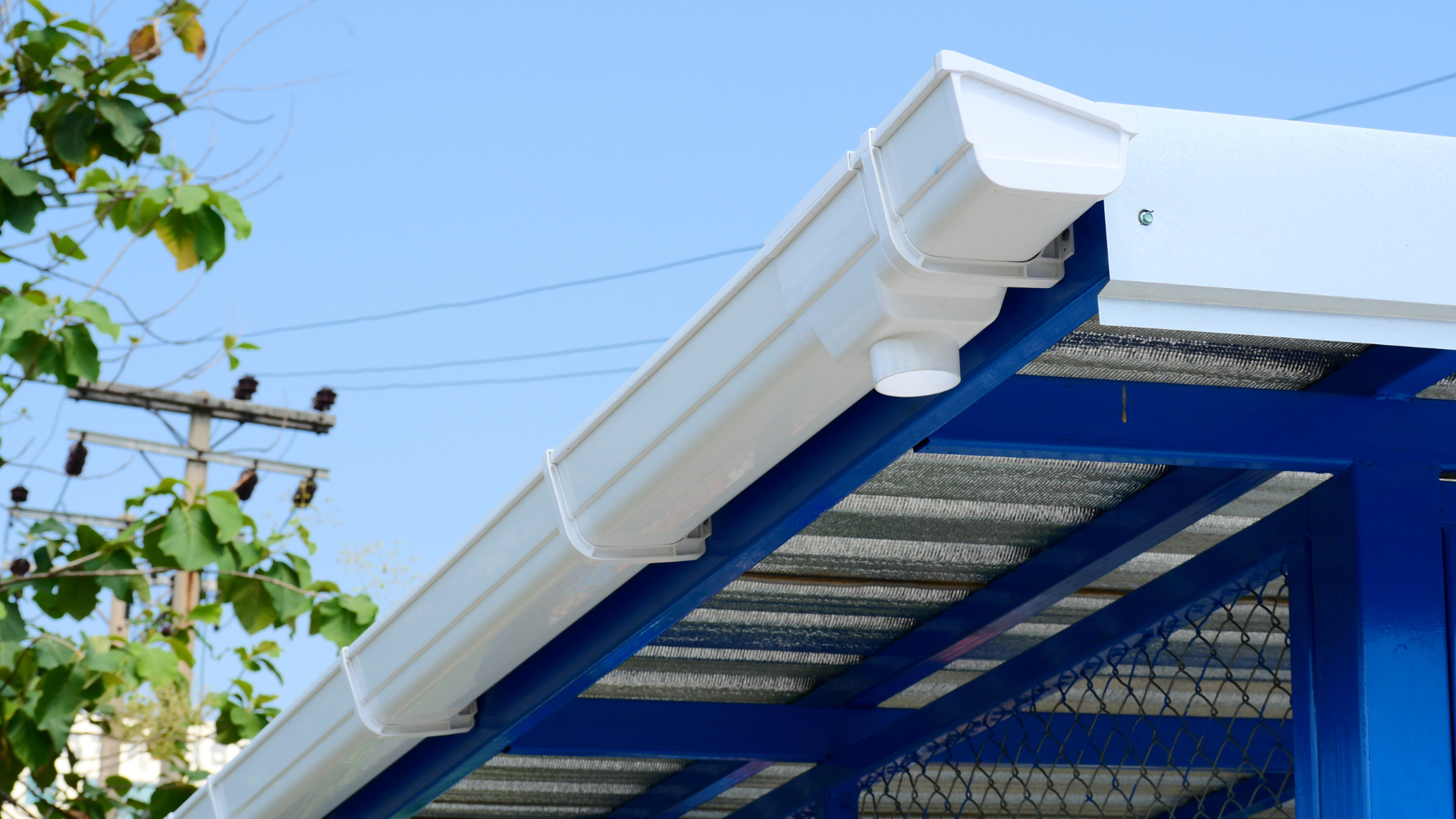 Person in a red jacket on a ladder cleaning a roof gutter against a blue sky