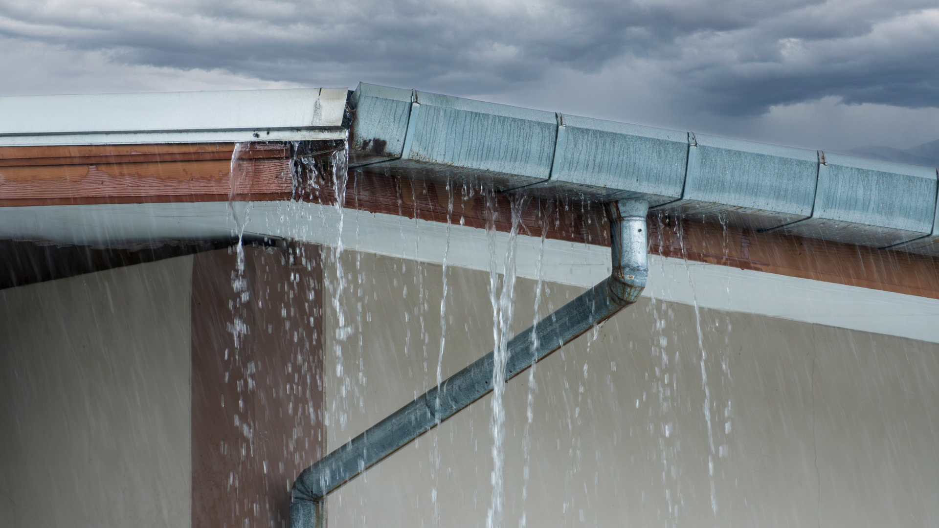 Rainwater pouring from a clogged gutter at the corner of a house roof