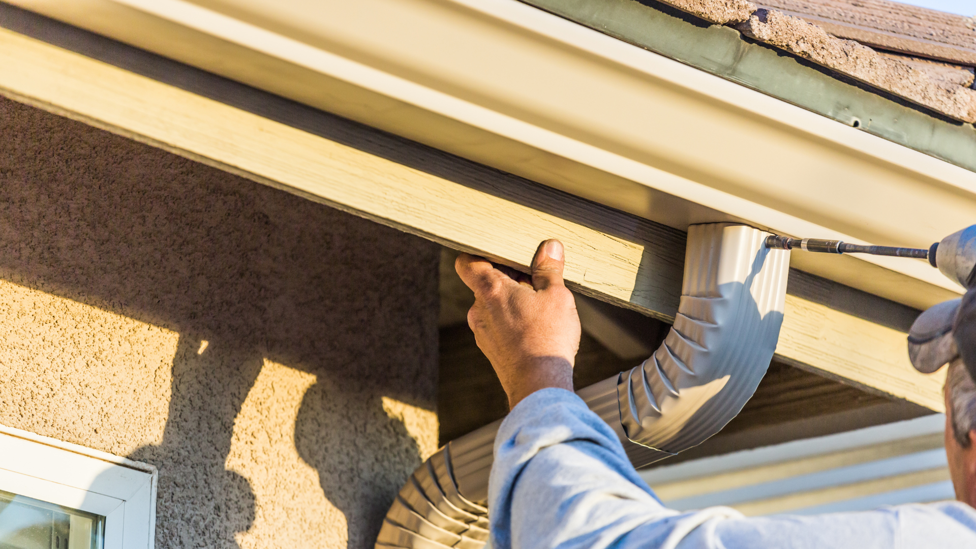 Handyman inspecting roof gutter under the eaves with a drill in hand