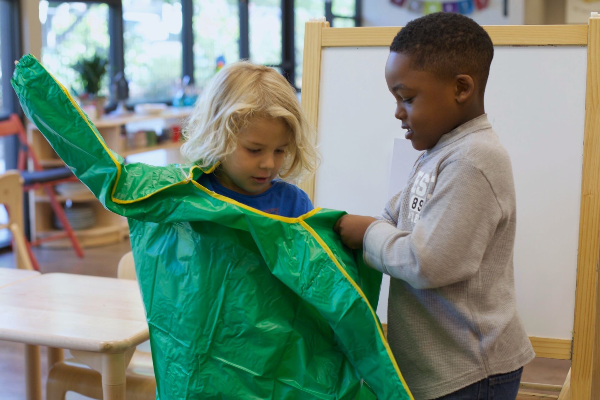 Two children examining a bright green costume or fabric in a classroom