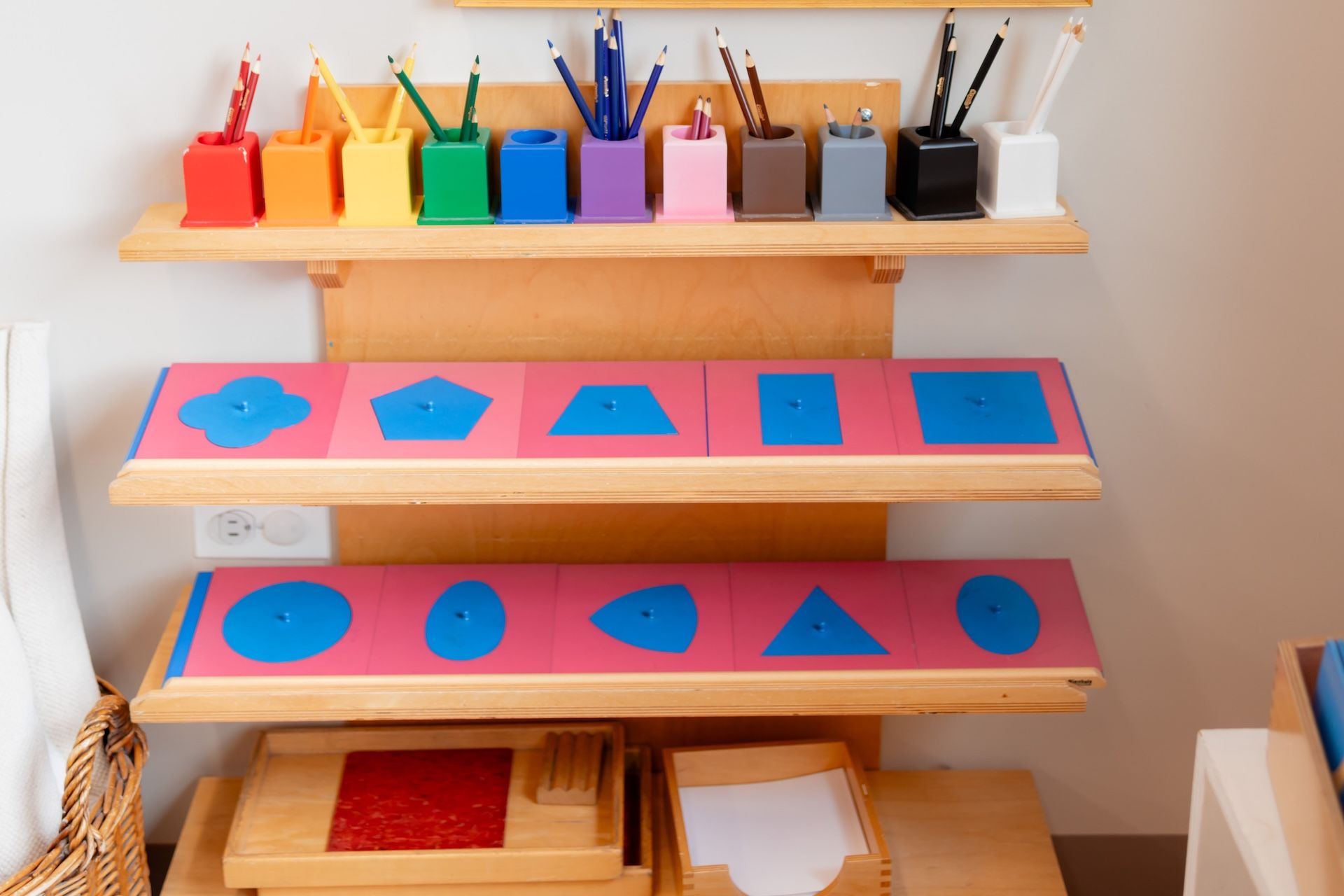 Colorful geometric shape sorting shelf with blue shapes on pink cards and markers in cups above
