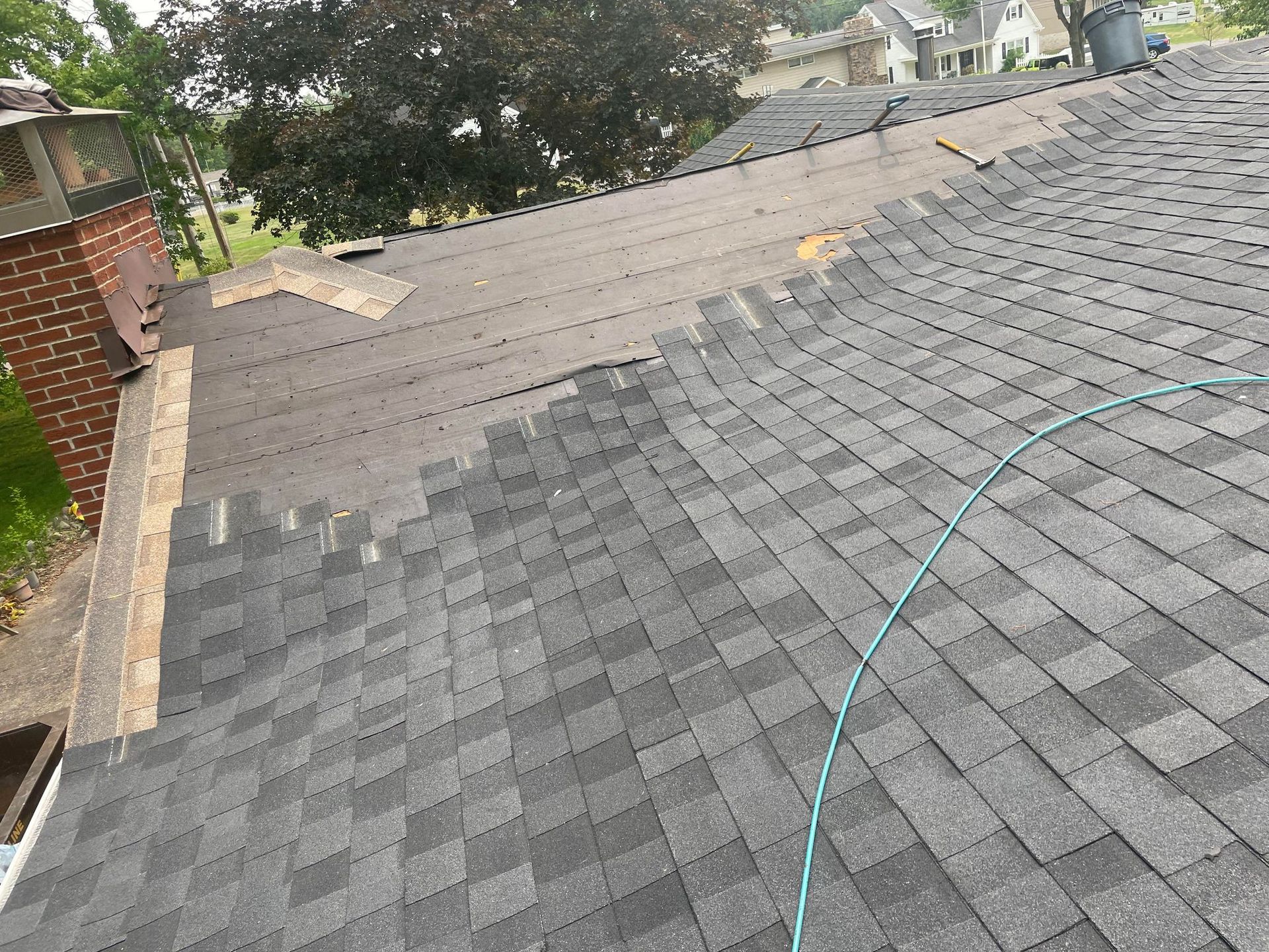 Roof partially re-shingled; gray shingles contrasted with exposed underlayment and chimney.