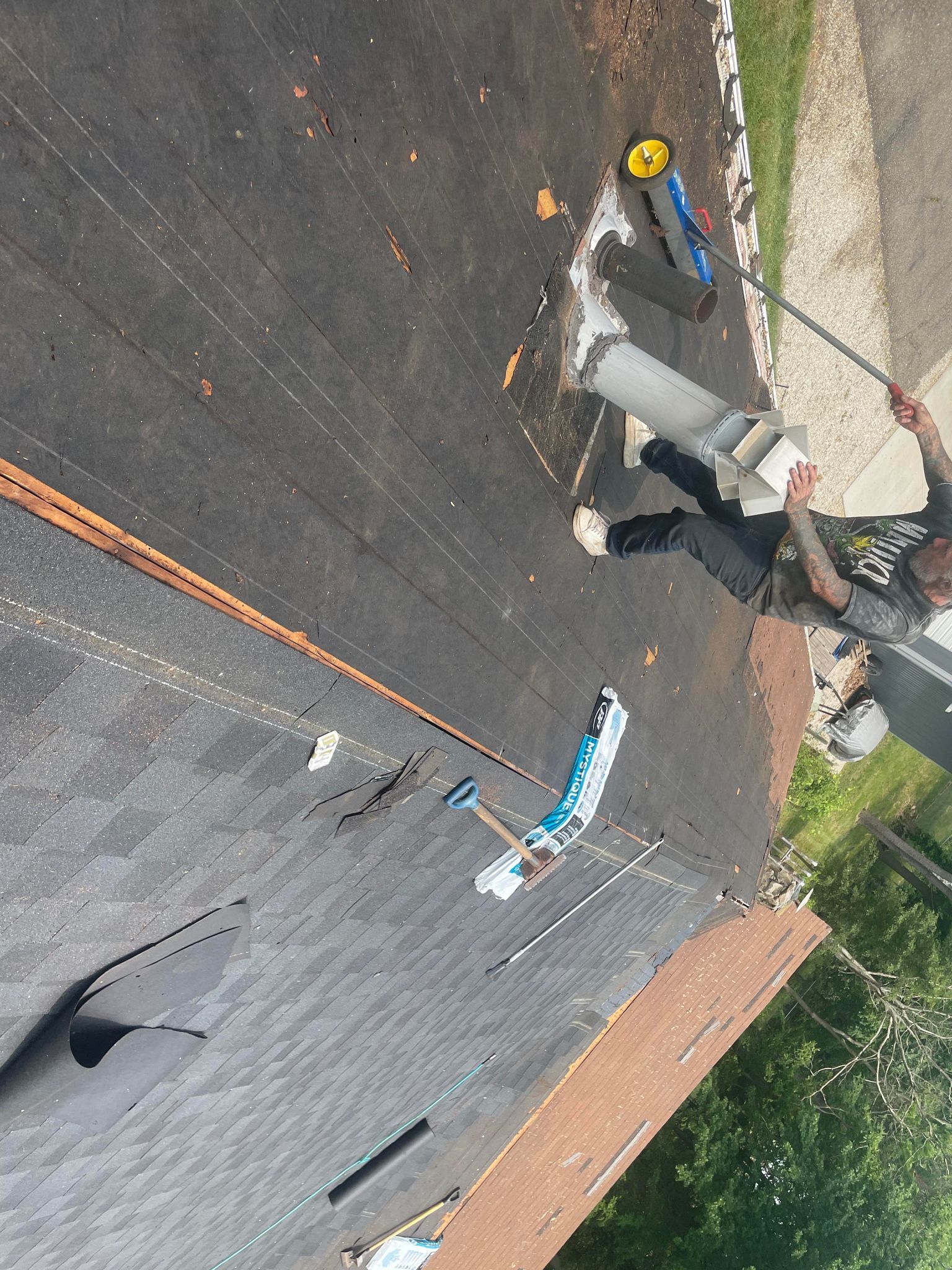 Person on rooftop pulls a cylindrical object up with a rope. Roof has tools and debris.