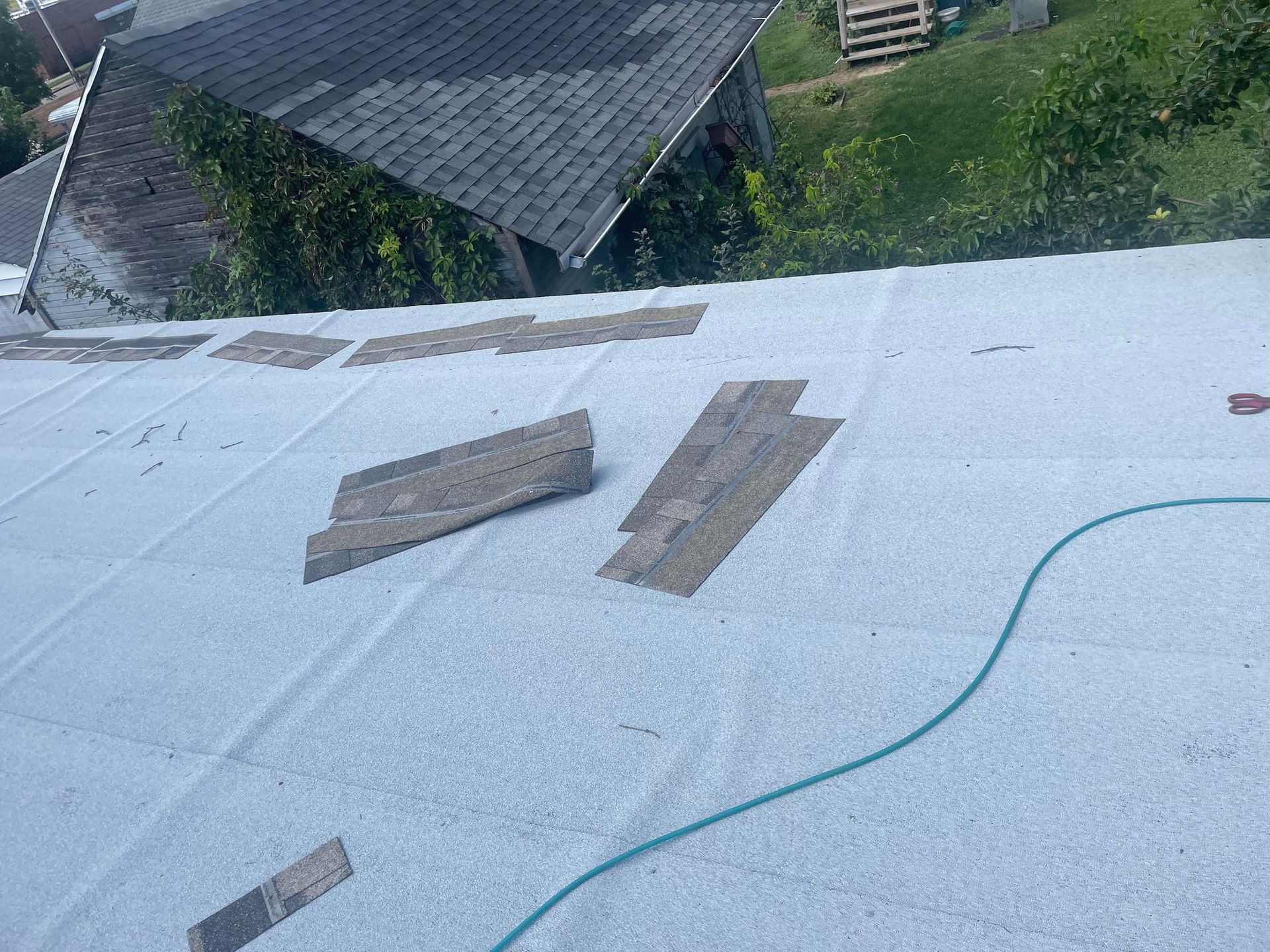 Flat roof with wooden planks on top, green hose, and background with a building and greenery.