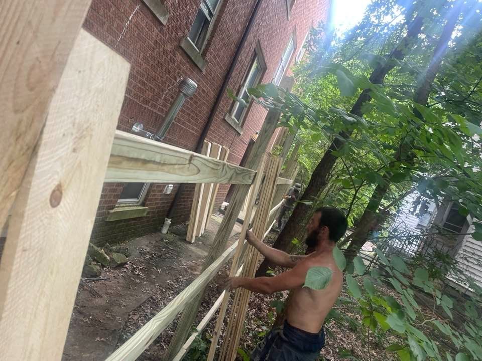 Person building wooden fence next to a brick building, outdoors.