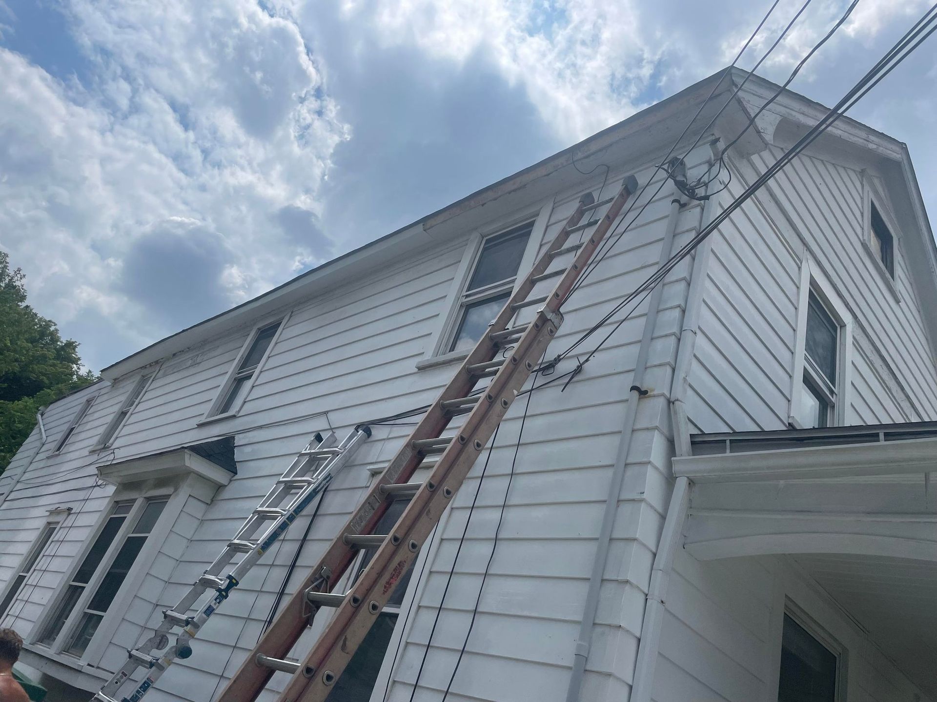 White house with multiple ladders set up, reaching the roof. Overcast sky.