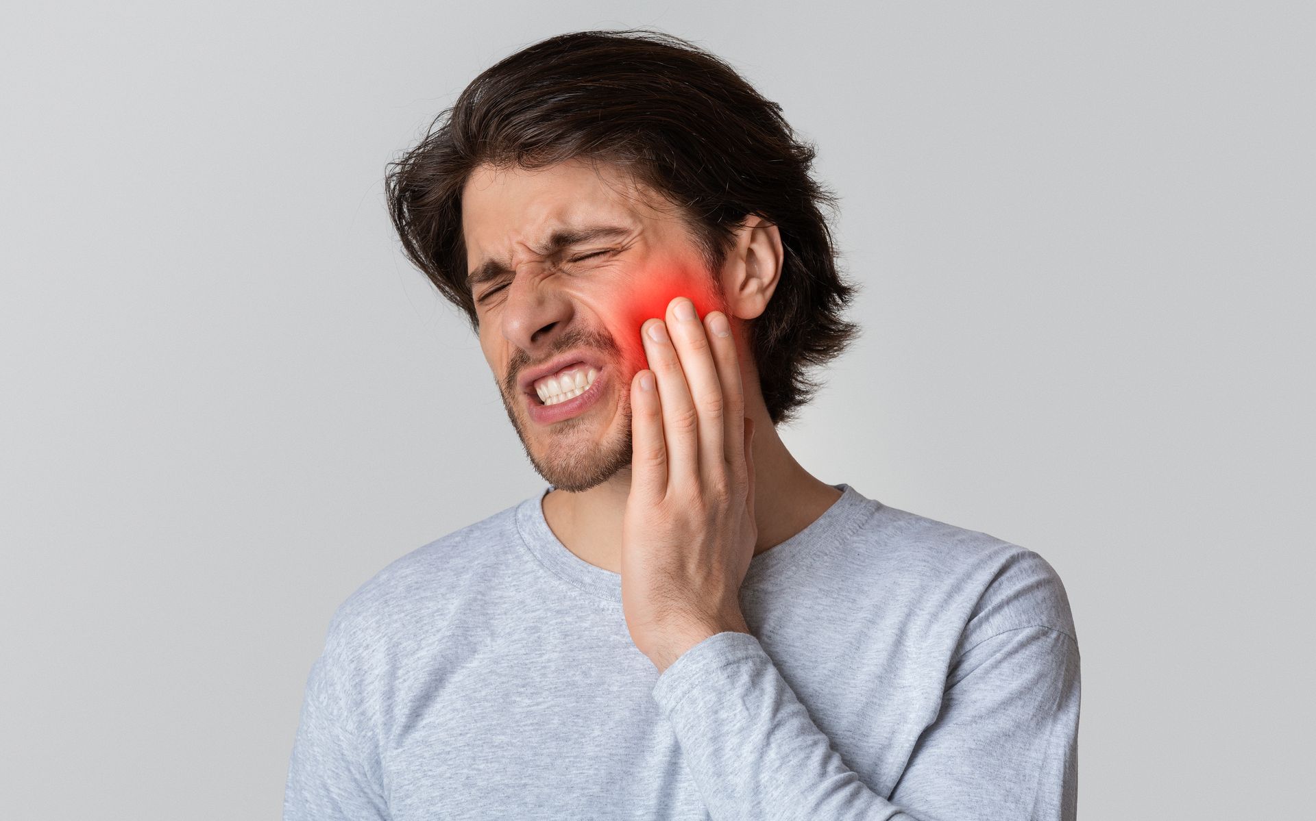 Man with painful expression, holding cheek near a red highlighted area, indicating toothache.