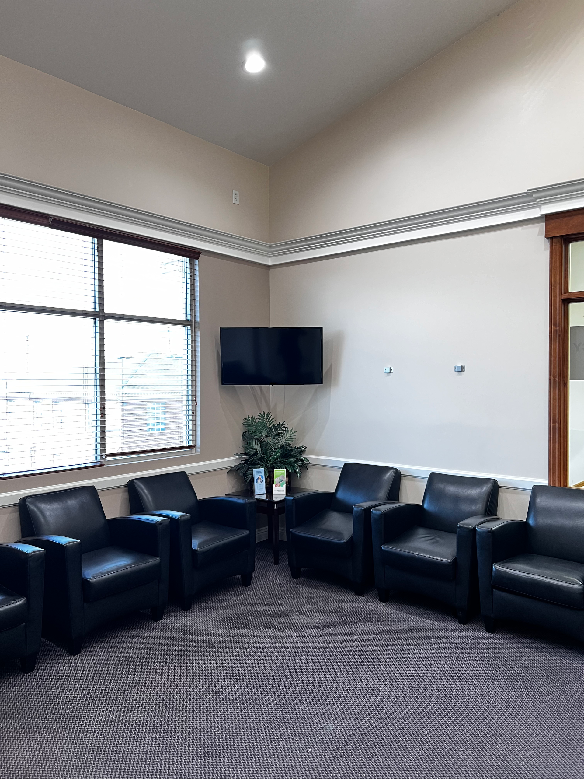 A waiting area with five black leather armchairs arranged in a semi-circle, a flat-screen TV, and patterned carpet.