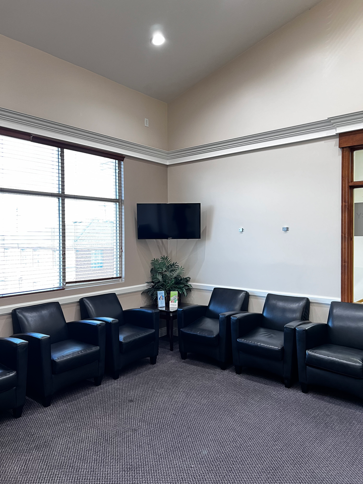A waiting area with five black leather armchairs arranged in a semi-circle, a flat-screen TV, and patterned carpet.