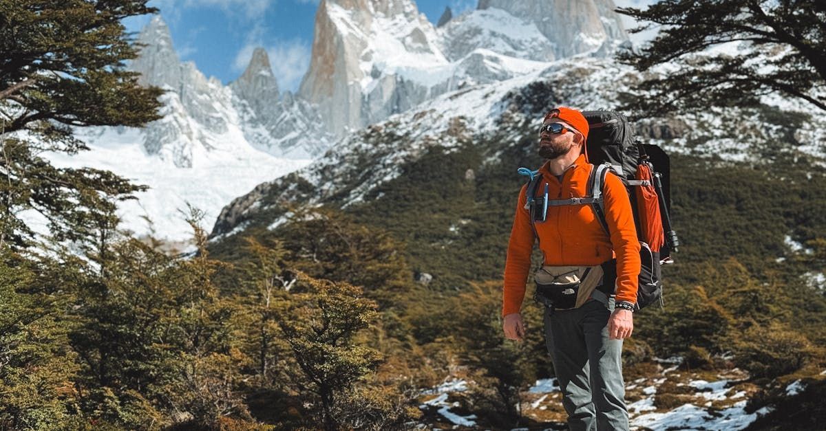 A man with a backpack is standing in front of a snowy mountain.
