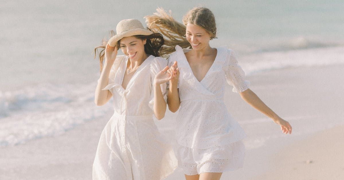Two women in white dresses are walking on the beach.
