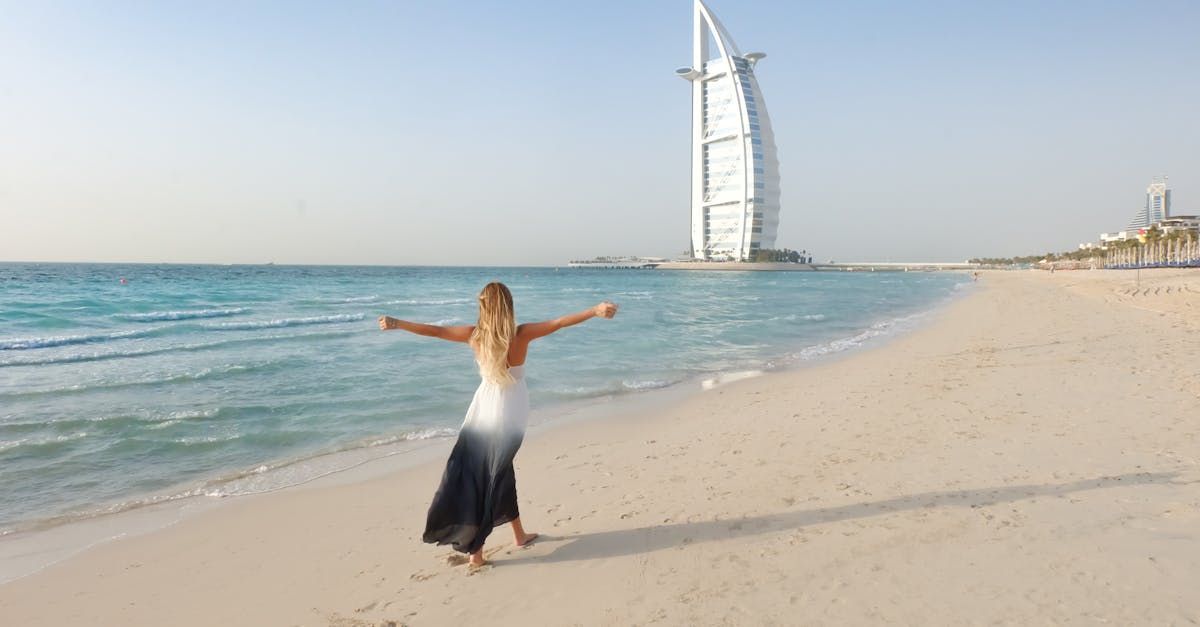 A woman is standing on a beach with her arms outstretched in front of a large building.