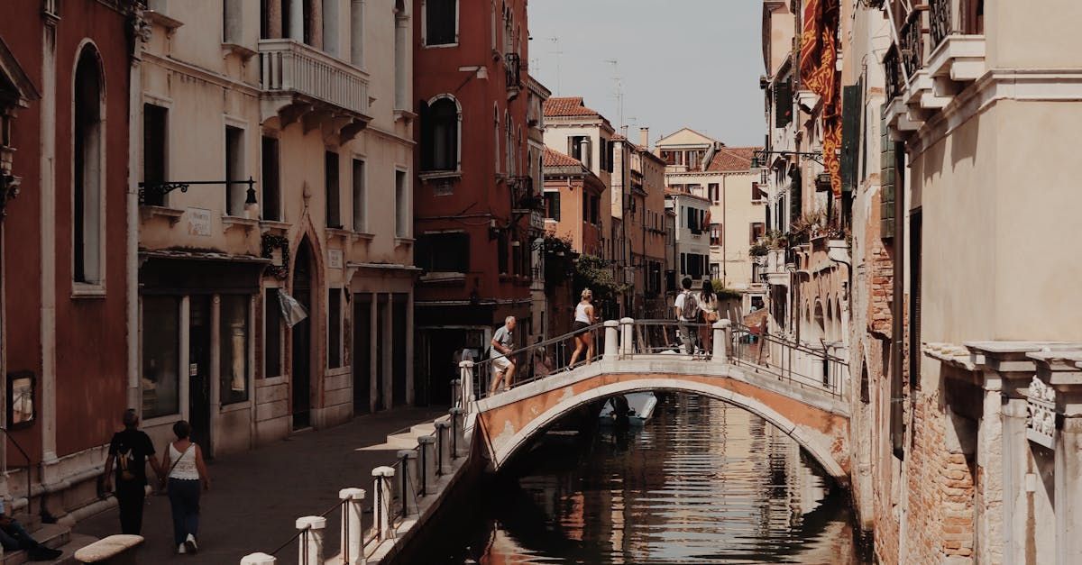 A canal in venice with a bridge over it and people walking on the sidewalk.