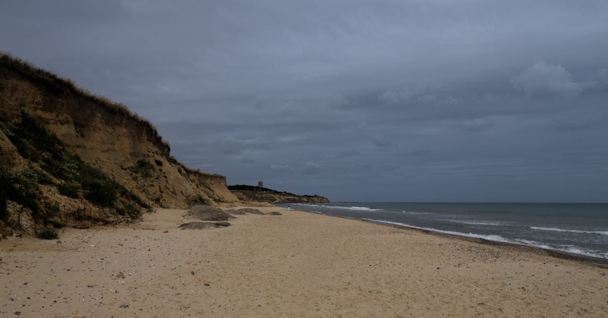A beach with a cliff and a body of water in the background on a cloudy day.
