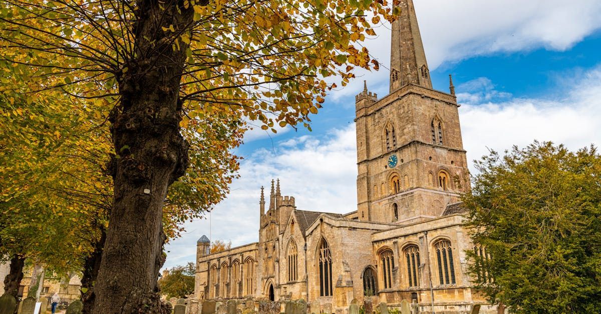 A large stone church with a clock tower and a tree in front of it.