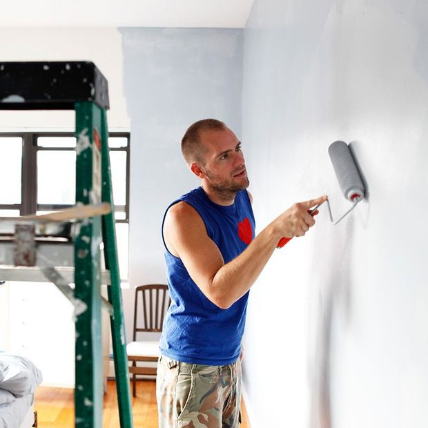 Man painting a wall blue with a paint roller; interior setting, green ladder.