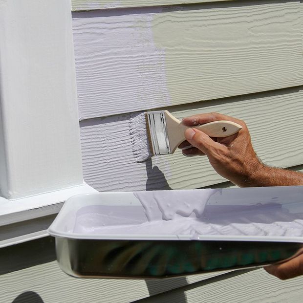 Hand painting siding with a brush, showing the color change from tan to lavender.