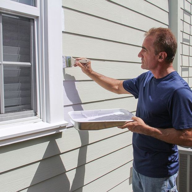 Man painting exterior trim of a house with a paintbrush and paint tray.