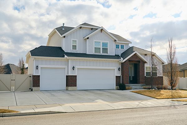 Two-story house with white siding, brick accents, and two-car garage under a cloudy sky.