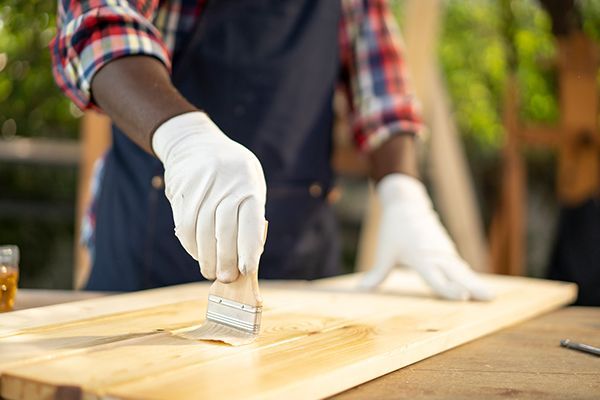 Person wearing gloves applying stain to a wooden board with a brush.