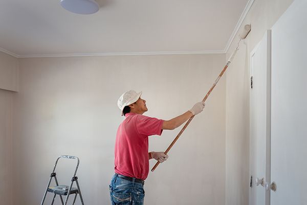 Person paints a white wall with a roller attached to an extension pole.