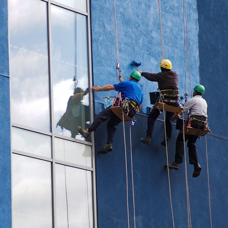Three window washers suspended from ropes painting a blue building. Three window washers suspended from ropes painting a blue building.