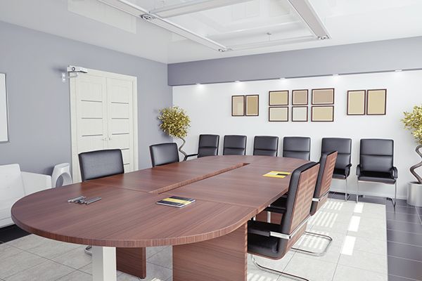 Conference room with large wooden table, black chairs, and framed artwork on white and gray walls.