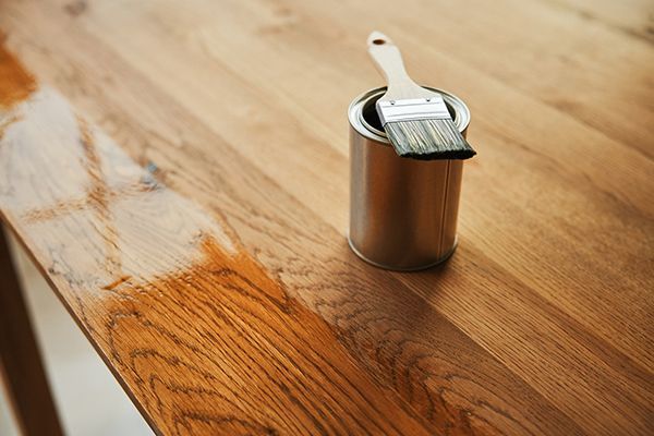 A partially varnished wooden table with a paint can and brush.