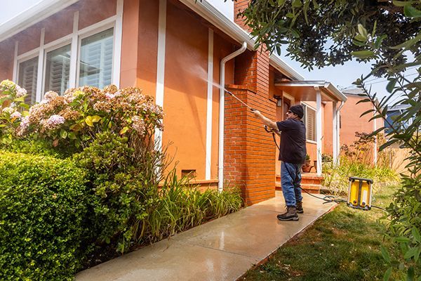 Man power washing an orange house exterior.