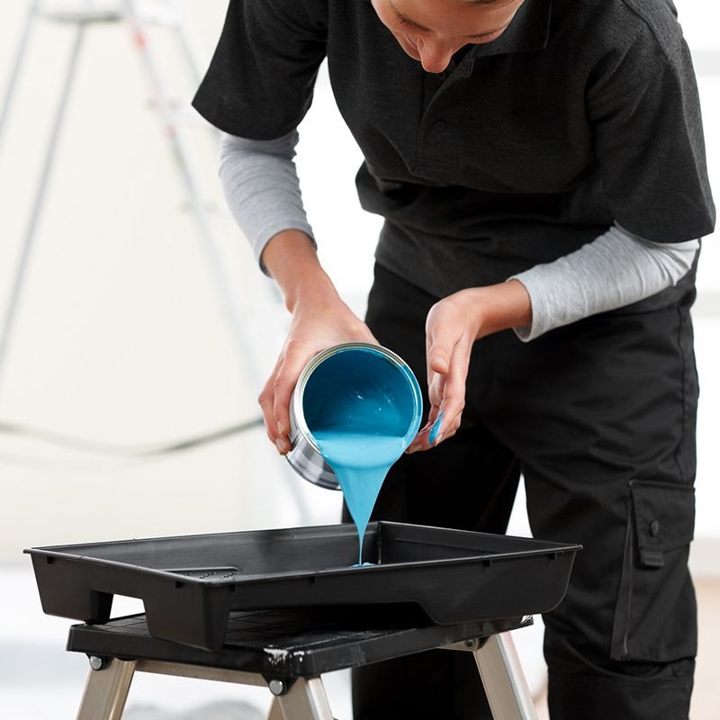 Person pouring turquoise paint from a can into a paint tray on a small step stool. Person pouring turquoise paint from a can into a paint tray on a small step stool.
