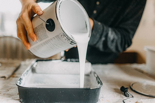 Person pouring white paint from a can into a paint tray, for home painting.