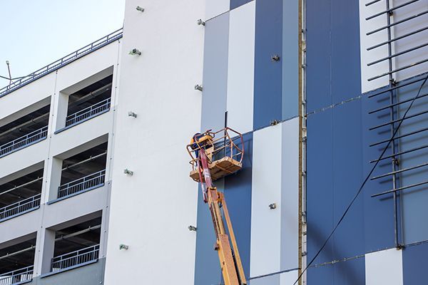 Worker in a lift installing panels on a multi-colored building exterior.