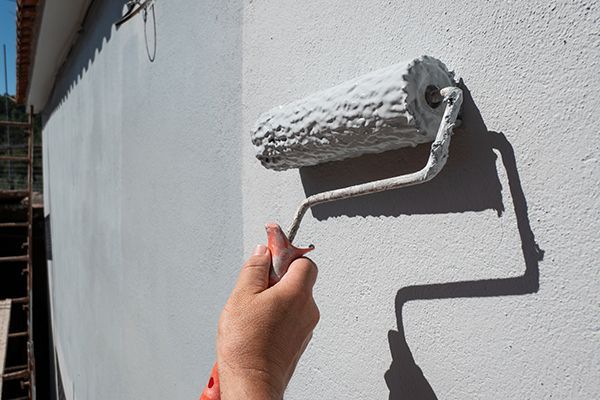 Hand using a paint roller on a gray wall.