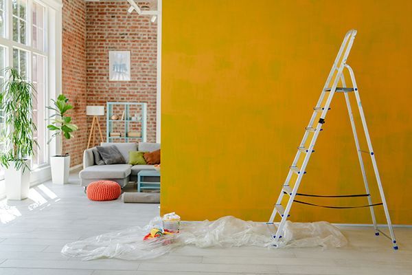 Ladder leaning against a bright yellow wall, in a living room being painted.