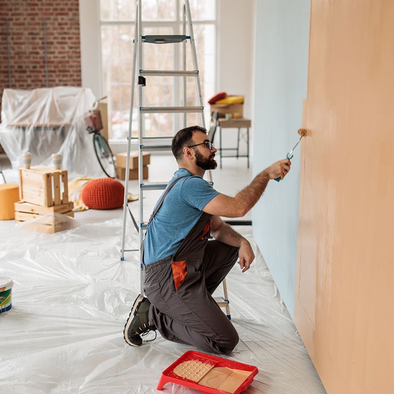 Man painting an interior wall with a paint roller while kneeling on plastic sheeting. Man painting an interior wall with a paint roller while kneeling on plastic sheeting.