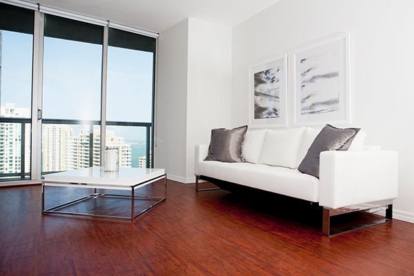 Modern living room with white sofa, coffee table, and large window overlooking a cityscape.