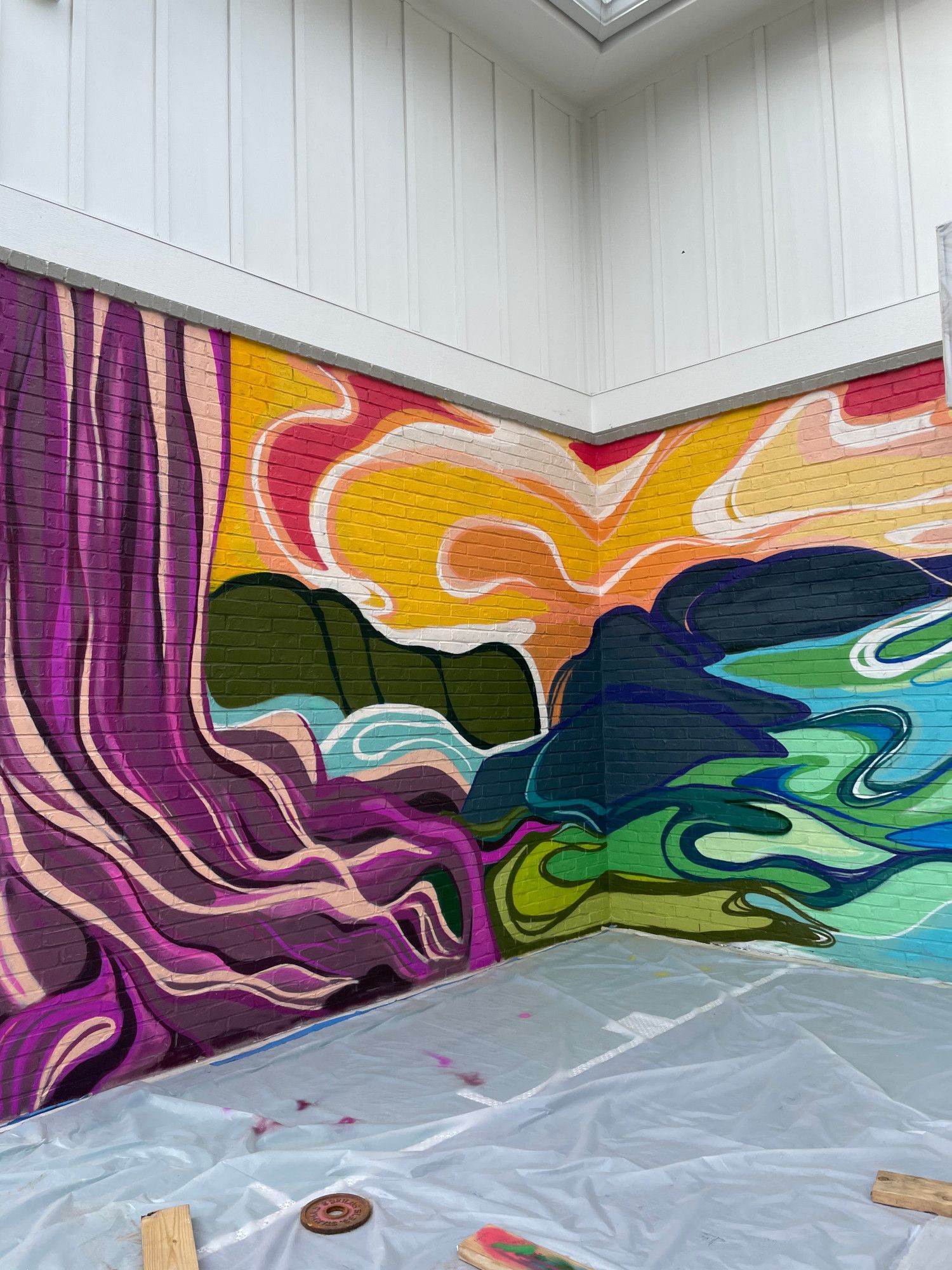 Mural on brick wall: Abstract landscape in purples, oranges, greens, and blues. Corner of a room.