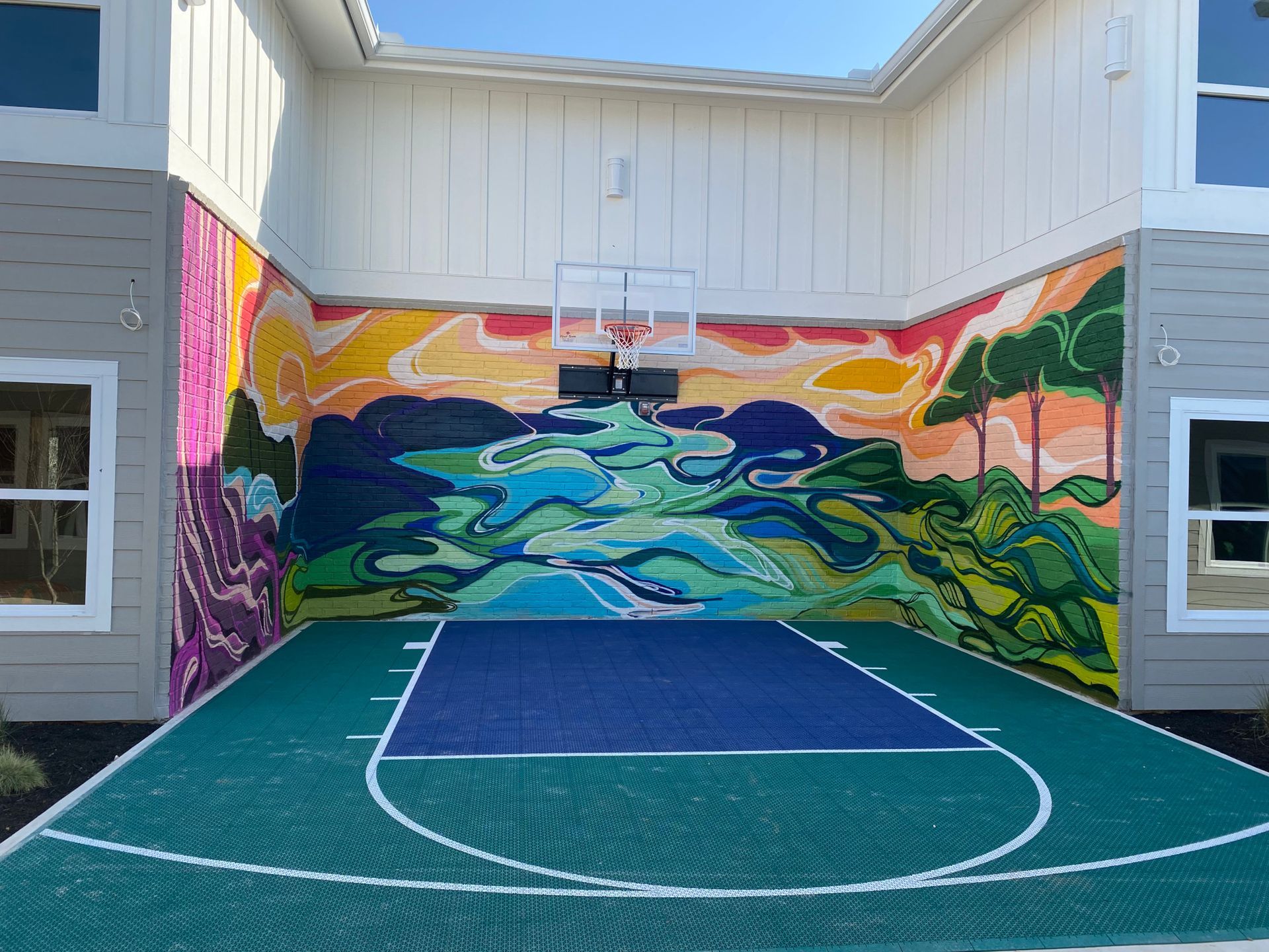 Basketball court with colorful mural backdrop, set between two buildings.