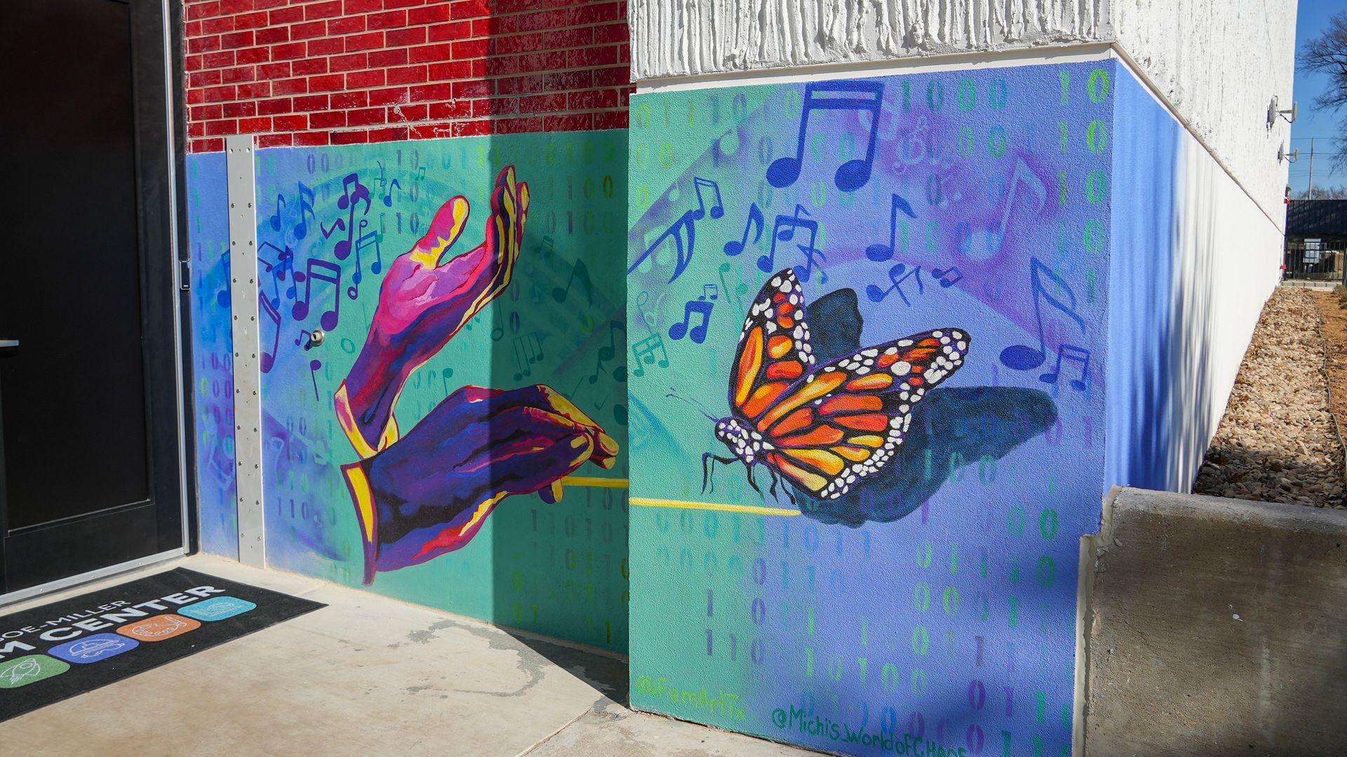 Mural of hands, a butterfly, and musical notes on a building corner. Bright colors include teal, purple, and orange.