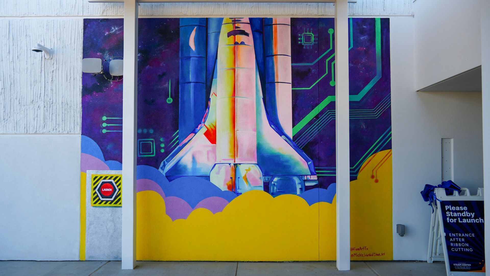 Mural of a space shuttle launching. Against a purple, blue and yellow background with clouds.