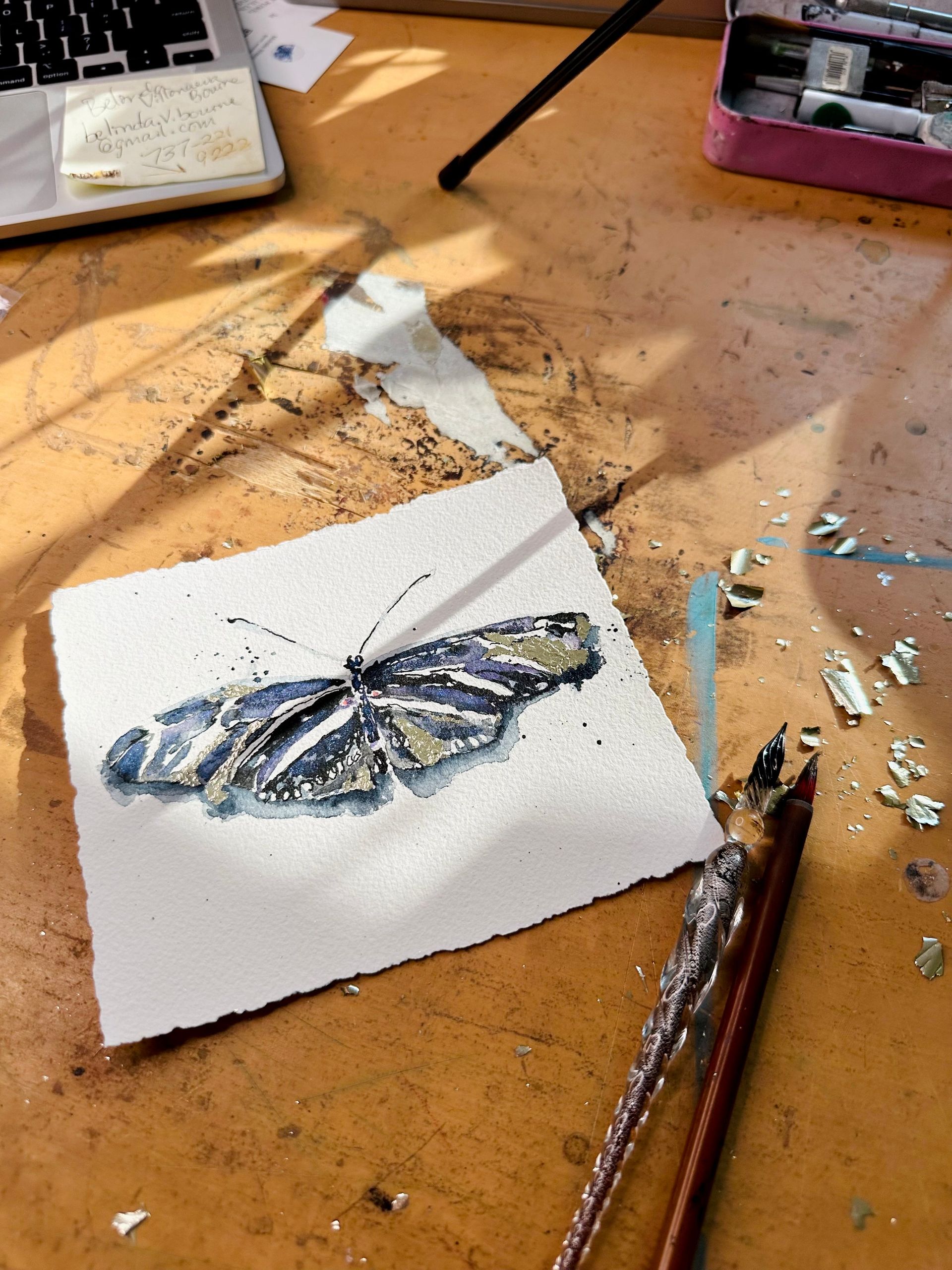 Butterfly watercolor painting on white paper, on a wooden table with art supplies.