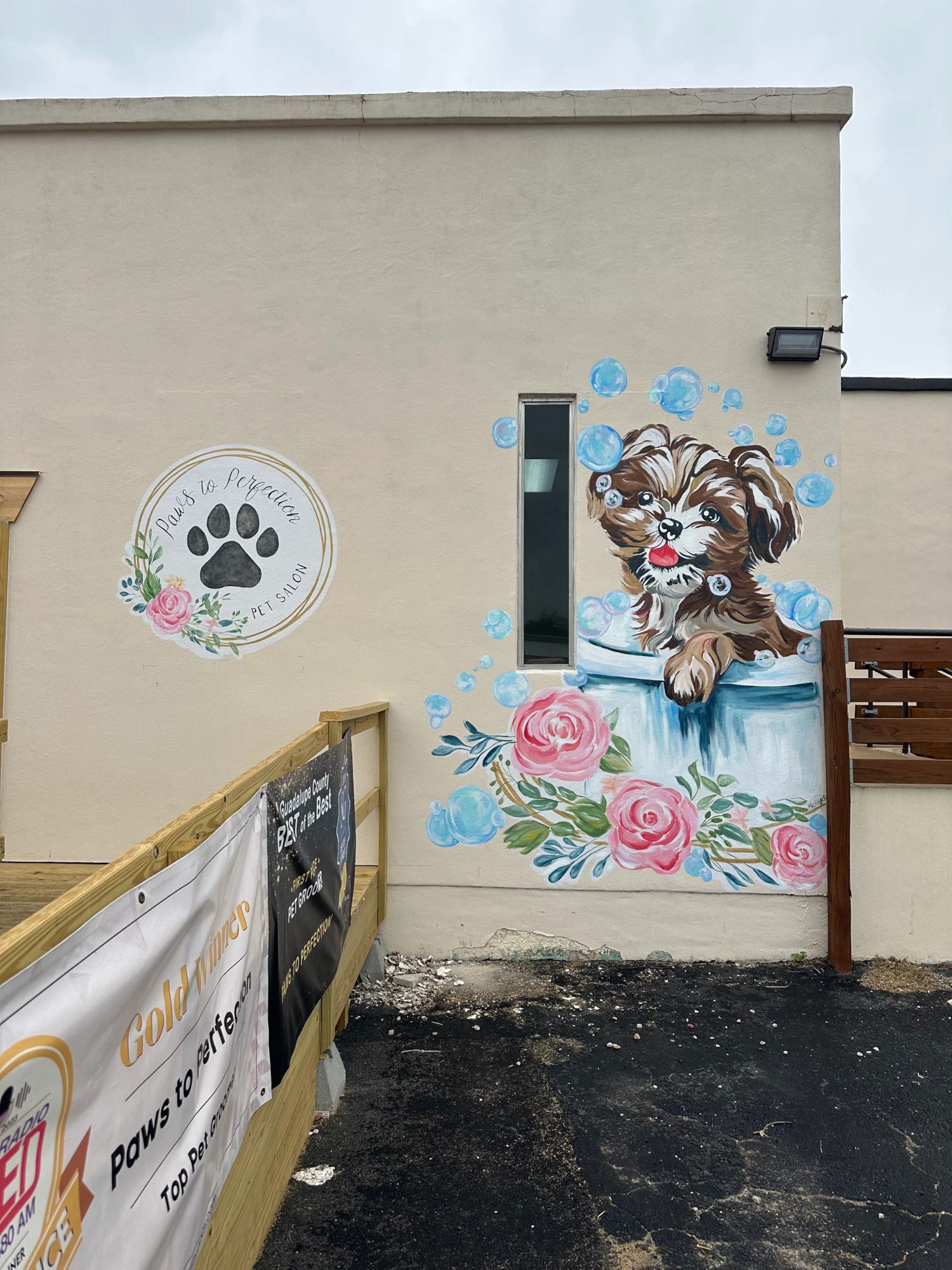 Mural on a tan building exterior, featuring a dog in a bathtub surrounded by flowers and paw print art.