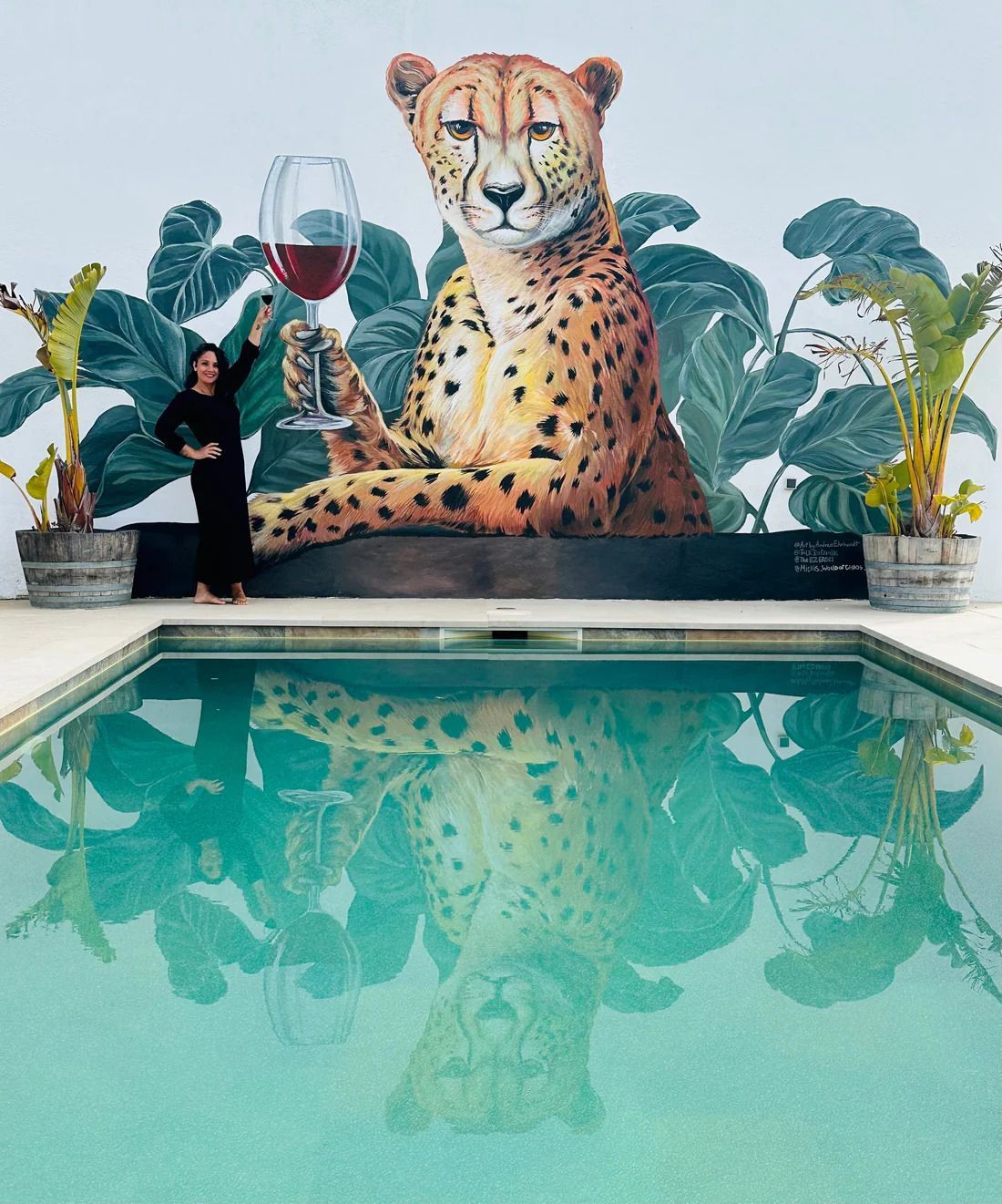 Woman holding wine glass by a pool, cheetah mural, and green foliage.