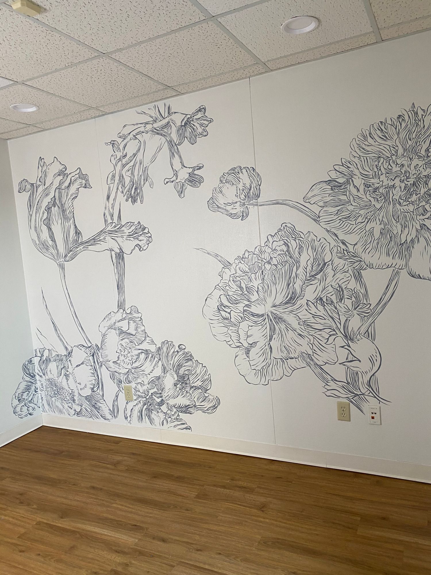 Floral line art mural on white wall in room with wood floor.