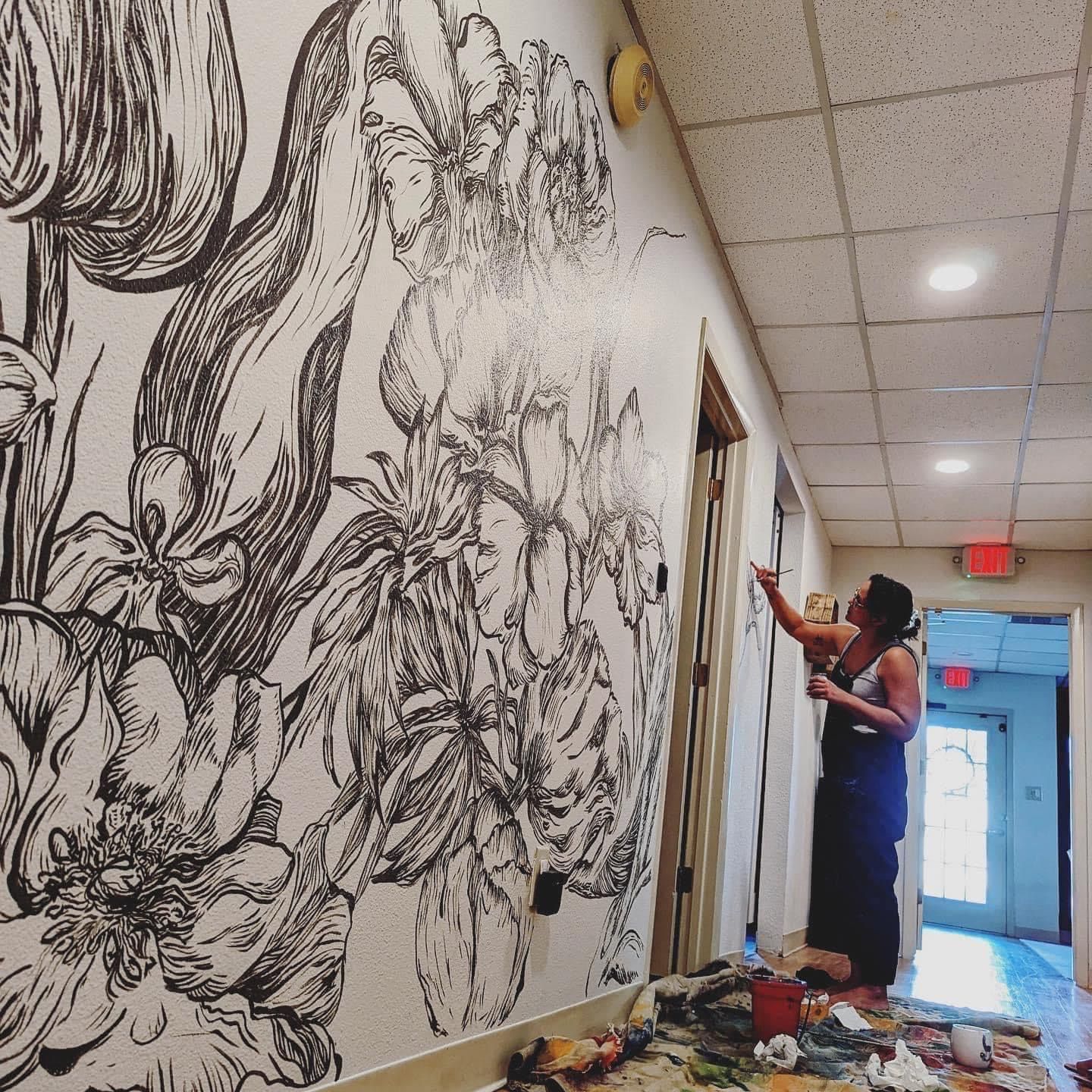 Woman painting large black and white floral mural in a hallway.