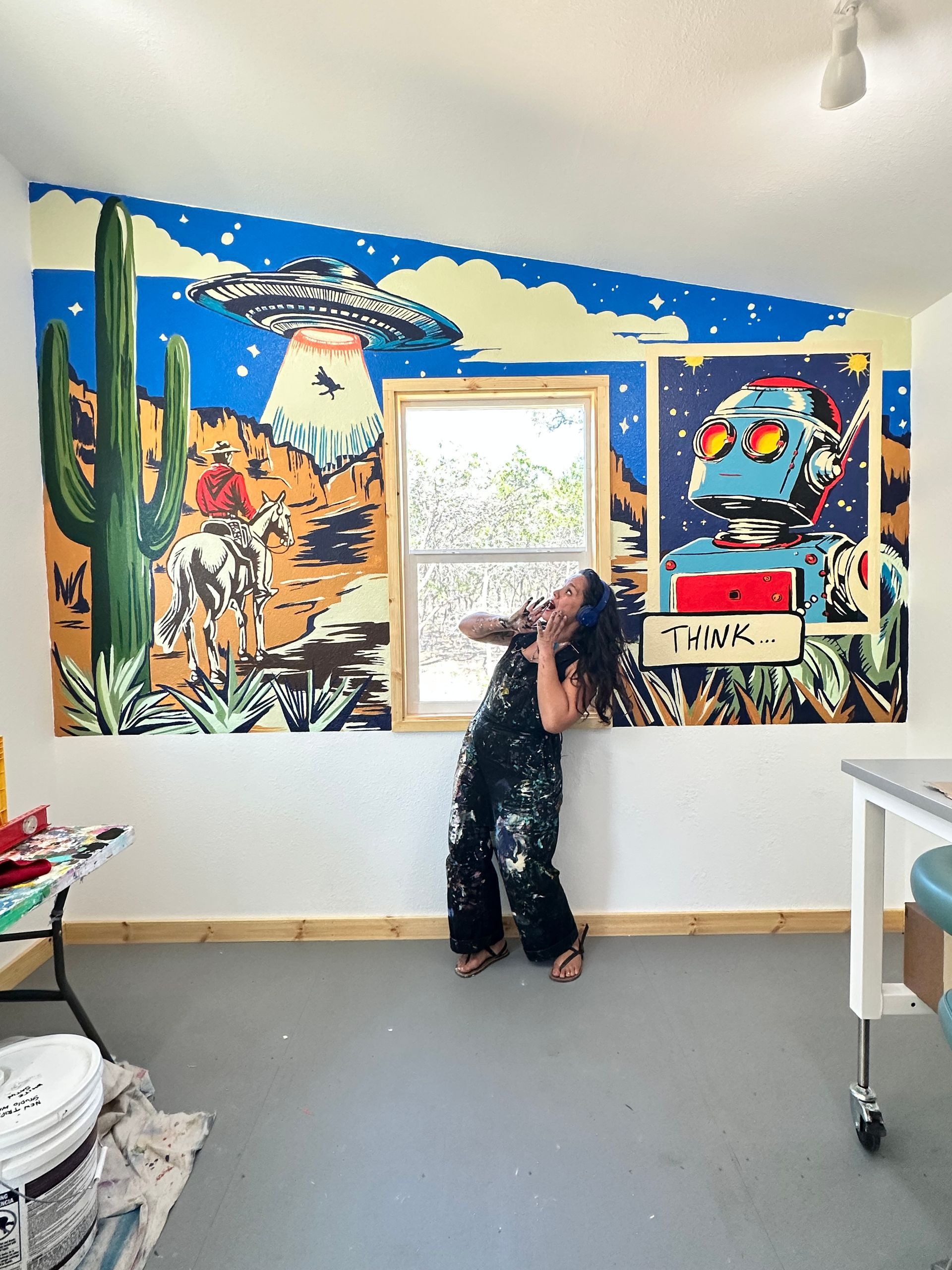 Person standing in a colorful room, facing a framed artwork on a painted mural wall.